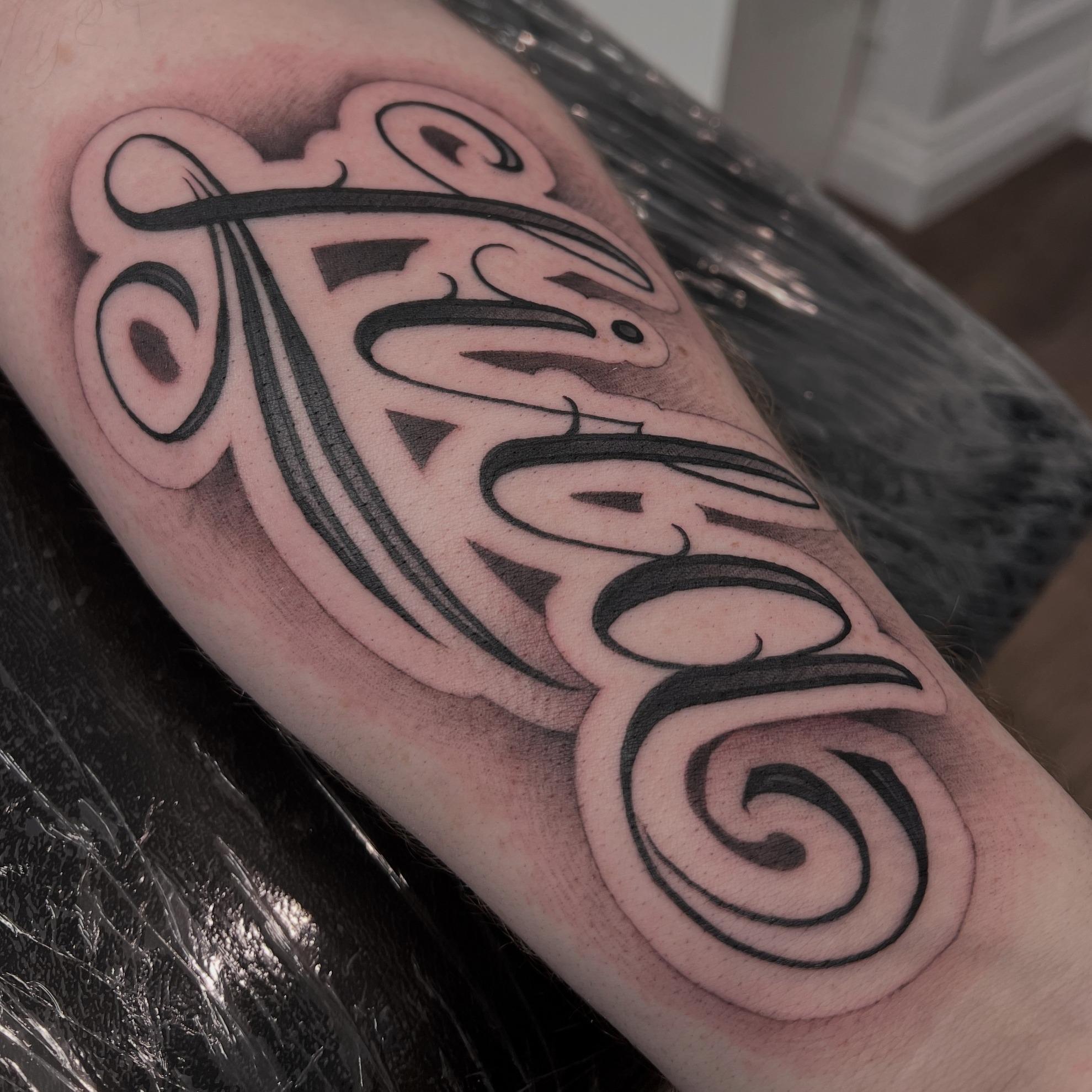 Bold shaded script lettering tattoo on the forearm by Independence Ink.