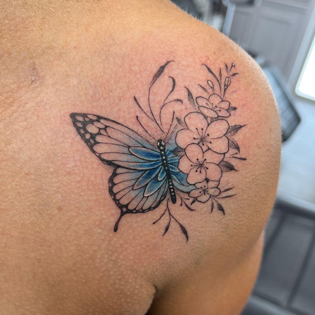 Butterfly and cherry blossom cover-up tattoo over old lettering on the shoulder by Independence Ink.
