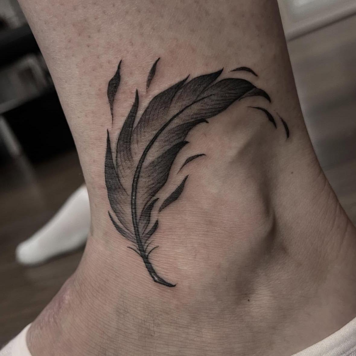 Soft black and grey feather tattoo above the ankle by Independence Ink.